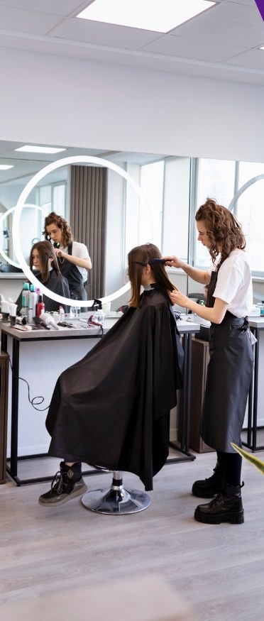 A hairdresser working on a client under ring-light mirrors